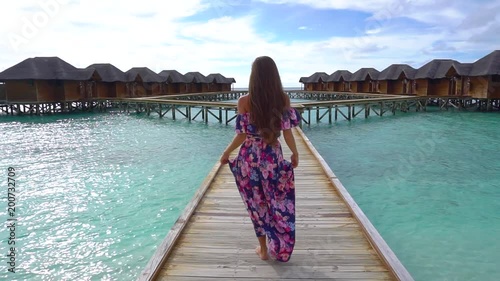 Female going on bridge on beach with transparent water of ocean in Maldives