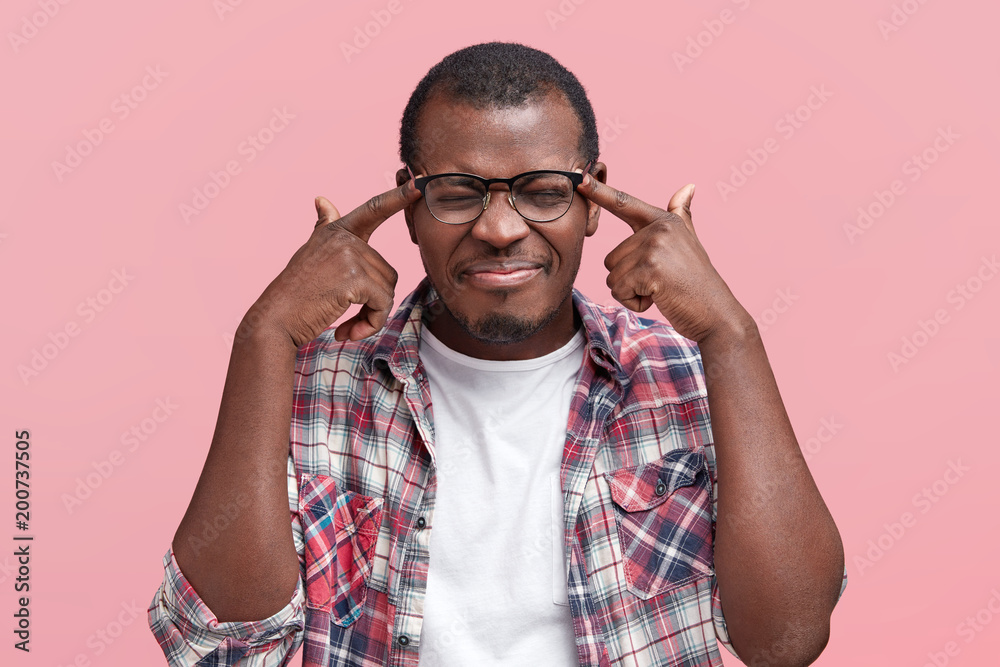 Fototapeta premium Worried depressed dark skinned male makes suicide gesture, pretends to shoot himself at temples, has many promblems in life, isolated over pink background. People, stress, depression concept