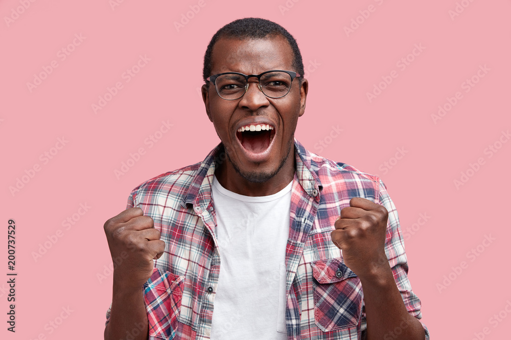 Mad furious man yells desprately at someone, clenches fists as can`t control emotions, shouts loudly and with anger, isolated over pink background. Negative human emotions and feelings concept Mad furious man yells desprately at someone, clenches fists as can`t control emotions, shouts loudly and with anger, isolated over pink background. Negative human emotions and feelings concept