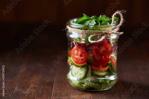 Creative vegetable salad served in glass jar over dark wooden background, selective focus, shallow depth of field