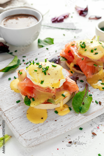 Eggs Benedict on english muffin with smoked salmon, lettuce salad mix and hollandaise sauce on white board photo