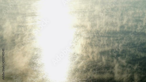 Water vapor on surface of cold icy water in river at sunny cold winter day. Close-up photo
