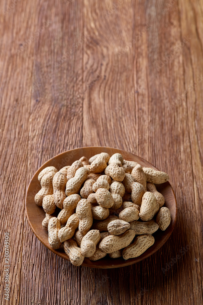 Unpeeled peanuts in wooden bowl over rustic wooden background closeup, selective focus Unpeeled peanuts in wooden bowl over rustic wooden background closeup, selective focus
