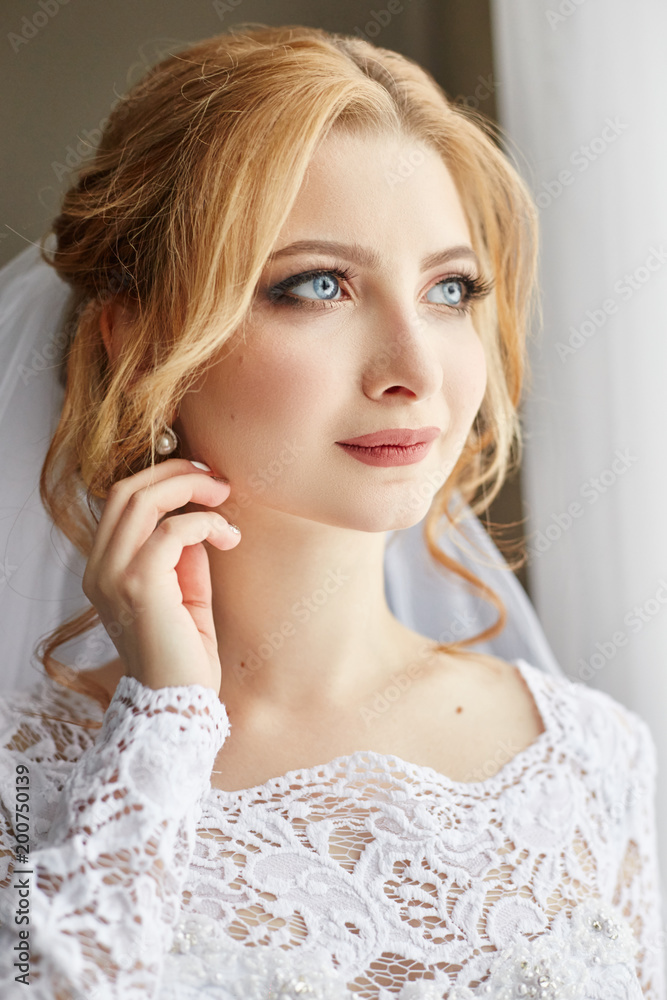 Beautiful blonde bride in the morning in a white wedding dress with veil on her head, portrait of the bride before the wedding ceremony. Brides experience before the wedding