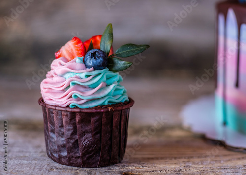 homemade cupcakes with pink and turquoise cream, decorated with strawberries and blueberries