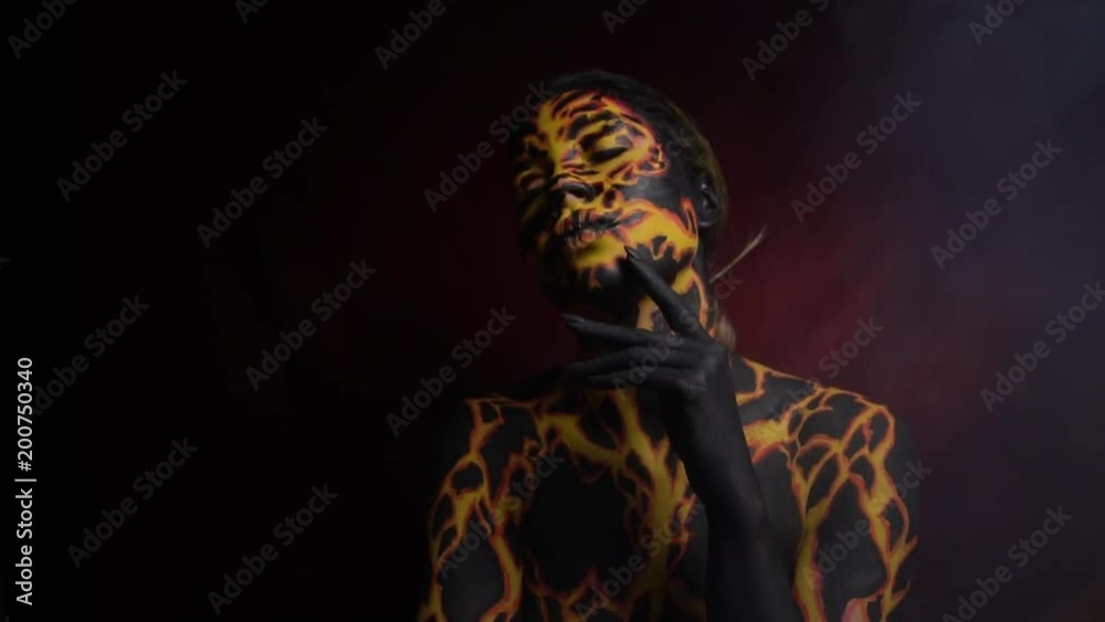 Body painting on the girl's body in the form of a current magma through the earth, which moves in a demonic dance in smoke on a red background Body painting on the girl's body in the form of a current magma through the earth, which moves in a demonic dance in smoke on a red background