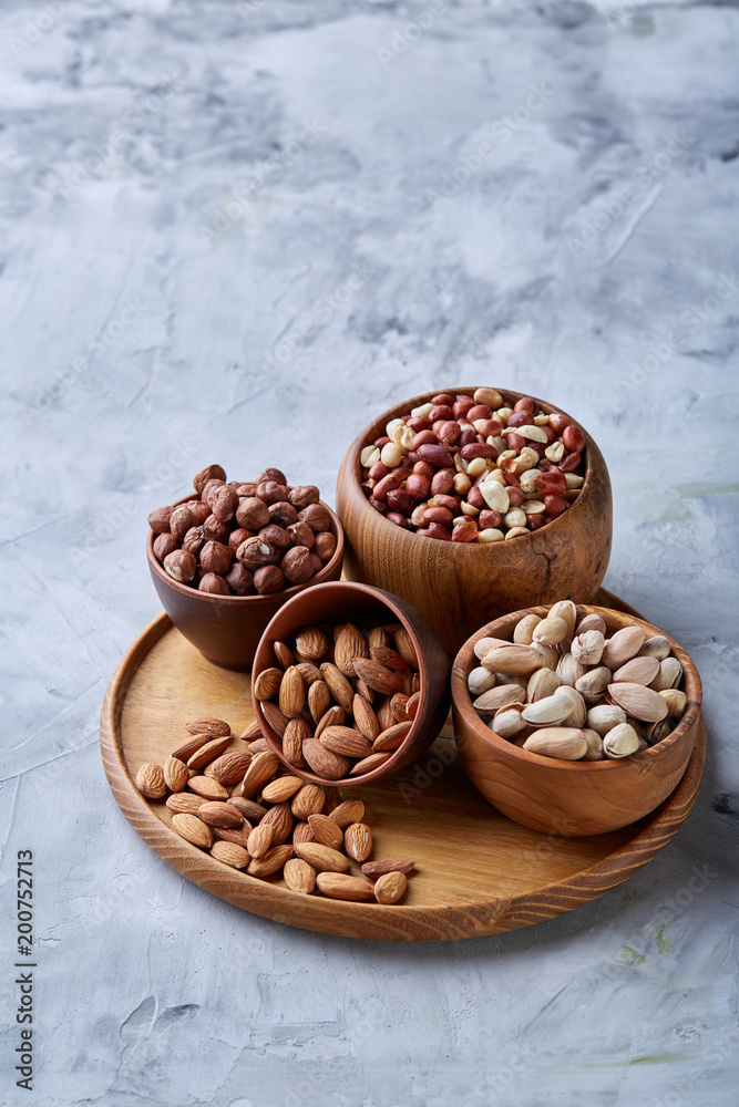 Mixed nuts in brown bowls on wooden tray over white background, close-up, top view, selective focus. Mixed nuts in brown bowls on wooden tray over white background, close-up, top view, selective focus.