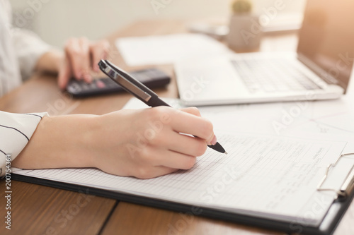 Closeup of woman hand writing in documents and using calculator