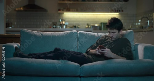 Man lying on a sofa at night using his mobile phone