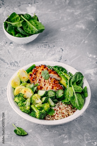 Healthy buddha bowl lunch with grilled chicken, quinoa, spinach, avocado, brussels sprouts, broccoli, cucumbers with sesame seeds