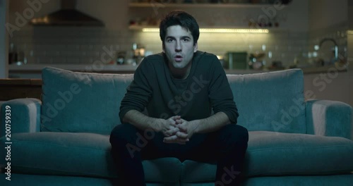 Man sitting on the edge of a sofa amazed and astonished by what he is watching.