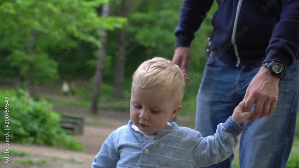 First steps of cute baby boy with father in park First steps of cute baby boy with father in park