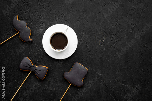Father's Day celebration concept. Monochrome. Cookies in shape of moustache, hat, bow tie near coffee on black background top view copy space