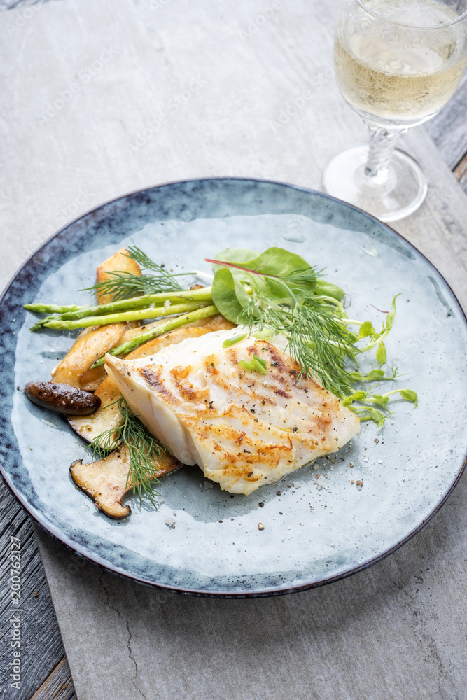 Fried cod fish filet with green asparagus and mushrooms as close up on a plate