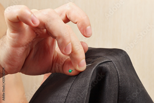 Hands of tailor pinned the pin to gray jacket close up