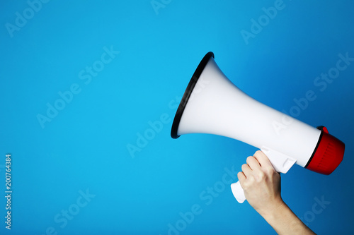 Female hand holding megaphone on blue background