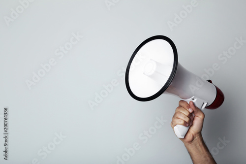 Female hand holding megaphone on grey background