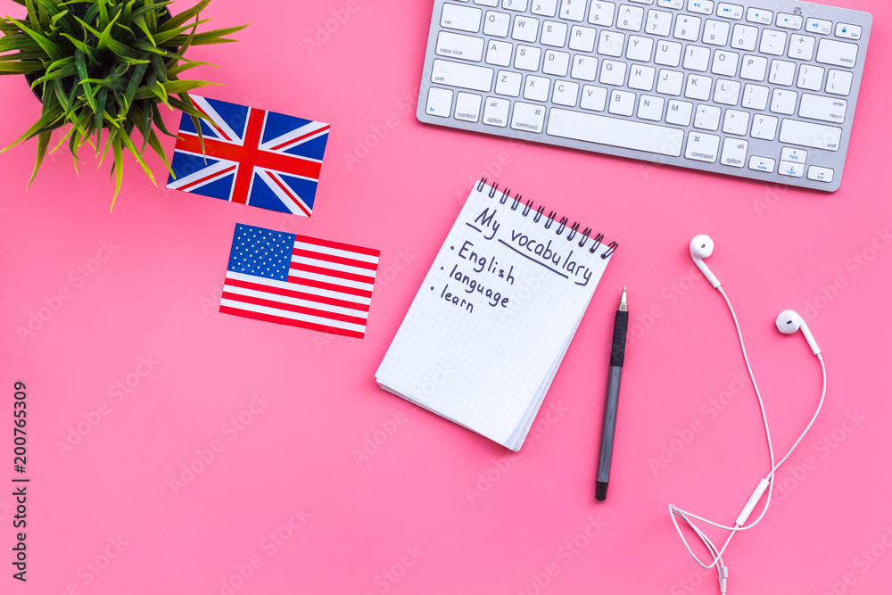 Fototapeta premium Learn english concept. British and american flags, computer keyboard, notebook for new vocabulary on pink background top view copy space