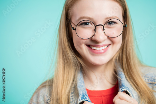 Close up portrait of beautiful smiling girl with glasses on blue background. Positive emotions, youthfulness of the concept