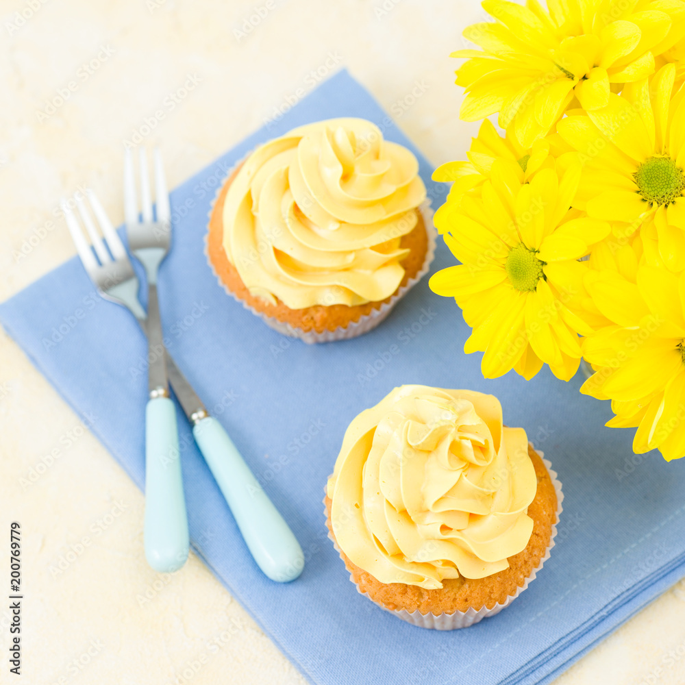 Cupcake with yellow cream decoration on blue napkin and bouquet of yellow chrysanthemum in small glass. Cupcake with yellow cream decoration on blue napkin and bouquet of yellow chrysanthemum in small glass.