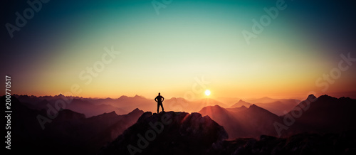 Man reaching summit enjoying freedom and looking towards mountains sunrise. photo