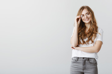 Top student in universite gets award. Cheerful beauitful blond girlfriend in trendy glasses, holding rim and smiling positively, hearing out stories of friends while standing over gray wall