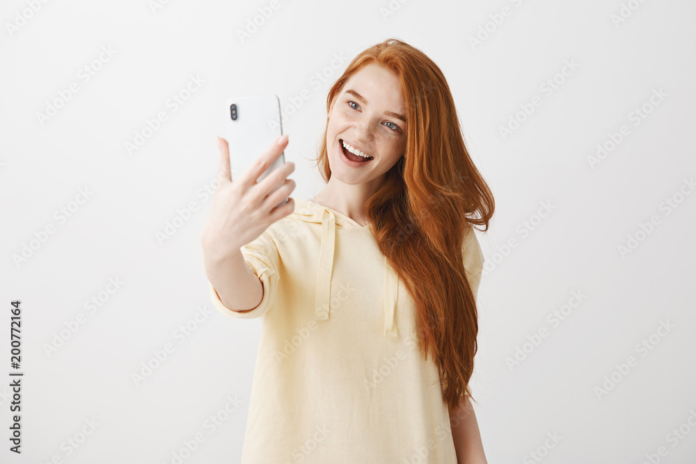 How about selfie. Portrait of attractive fashionable female blogger with natural red hair, posing while pulling hand with smartphone and taking photo of herself, sending picture to followers How about selfie. Portrait of attractive fashionable female blogger with natural red hair, posing while pulling hand with smartphone and taking photo of herself, sending picture to followers