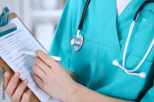 Fotografi Female doctor filling up medical form on clipboard closeup