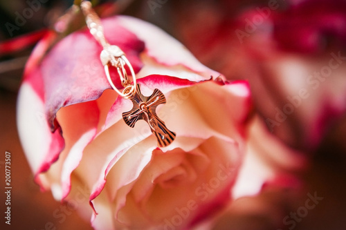 golden cross is hanging on the background of a rose