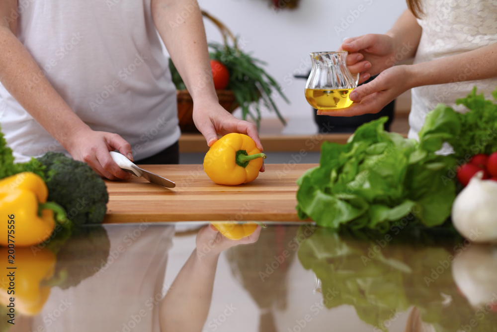 Closeup of human hands cooking in kitchen. Mother and daughter or two female cutting bell pepper for fresh salad. Healthy meal, vegetarian food and lifestyle concepts