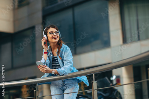 Young woman listens to music via headphones and smartphone in the city