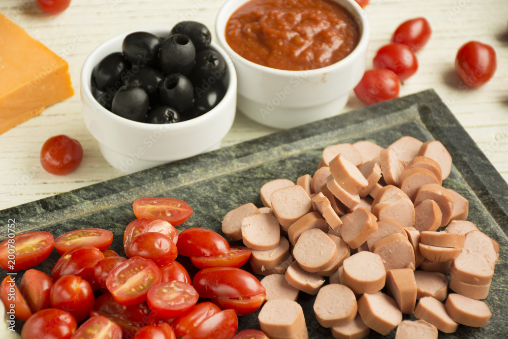 Ingredients for Italian pizza with cheddar cheese, mushrooms, black olives and sausage on white wooden background 