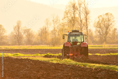 Farmer plowing soil at sunset in spring time