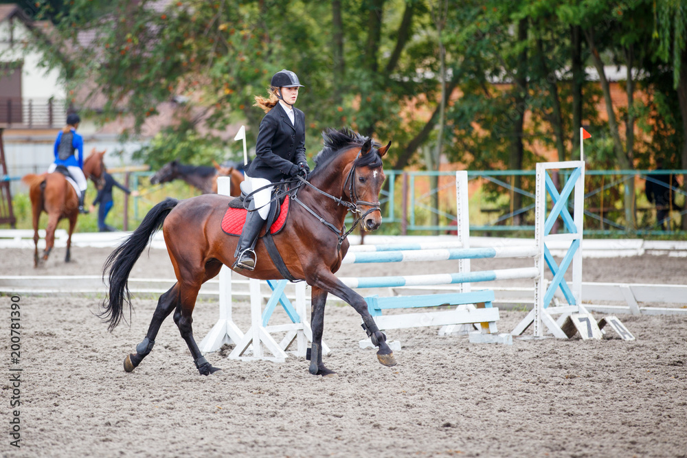 Young girl riding bay horse on show jumping competition Young girl riding bay horse on show jumping competition