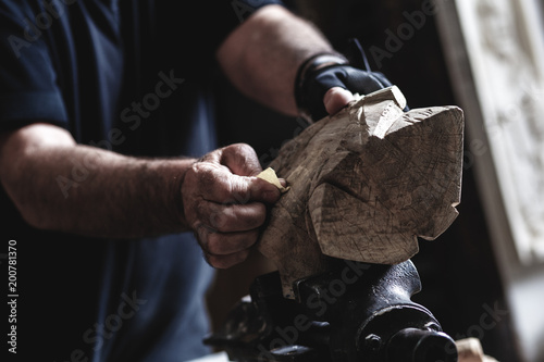 Senior man working on his wooden sculpture with sandpaper in his workshop.
