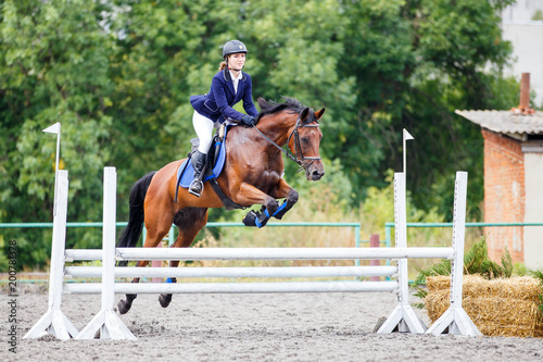 Young girl riding sorrel horse on show jumping competition