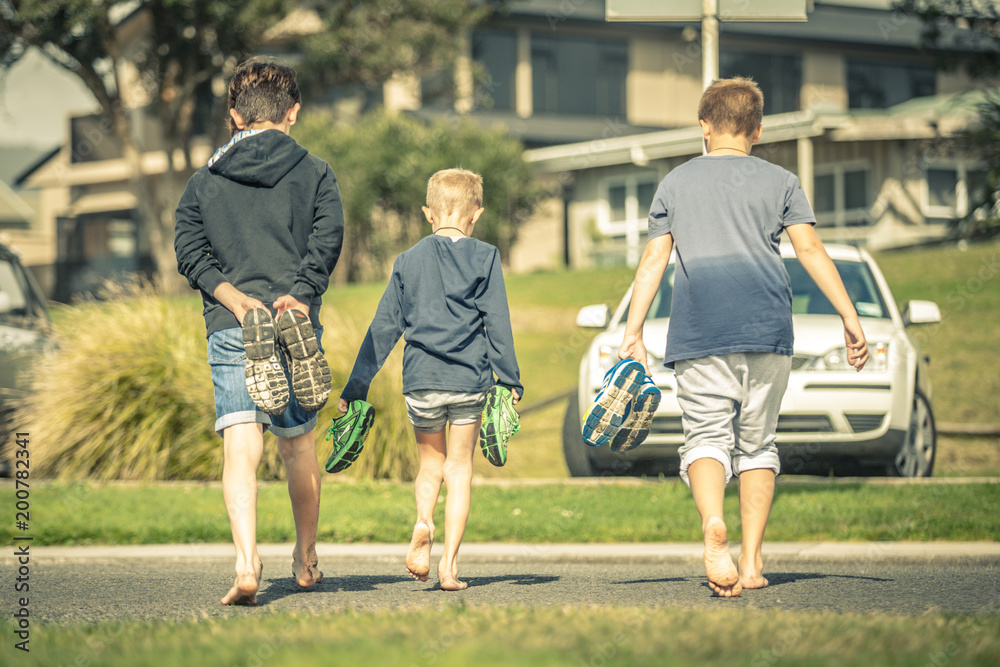Three boys walking barefoot on the street in New Zealand. Friends enjoying  a sunny day with