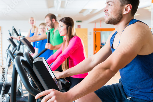 Male and female athletes doing spinning on home trainers in health club gym