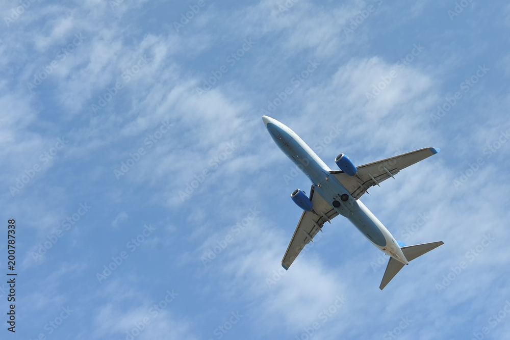 The passenger plane flies low overhead on a blue sky background. Bottom view The passenger plane flies low overhead on a blue sky background. Bottom view