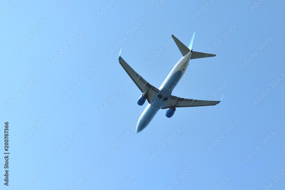 The passenger plane flies low overhead on a blue sky background. Bottom view The passenger plane flies low overhead on a blue sky background. Bottom view