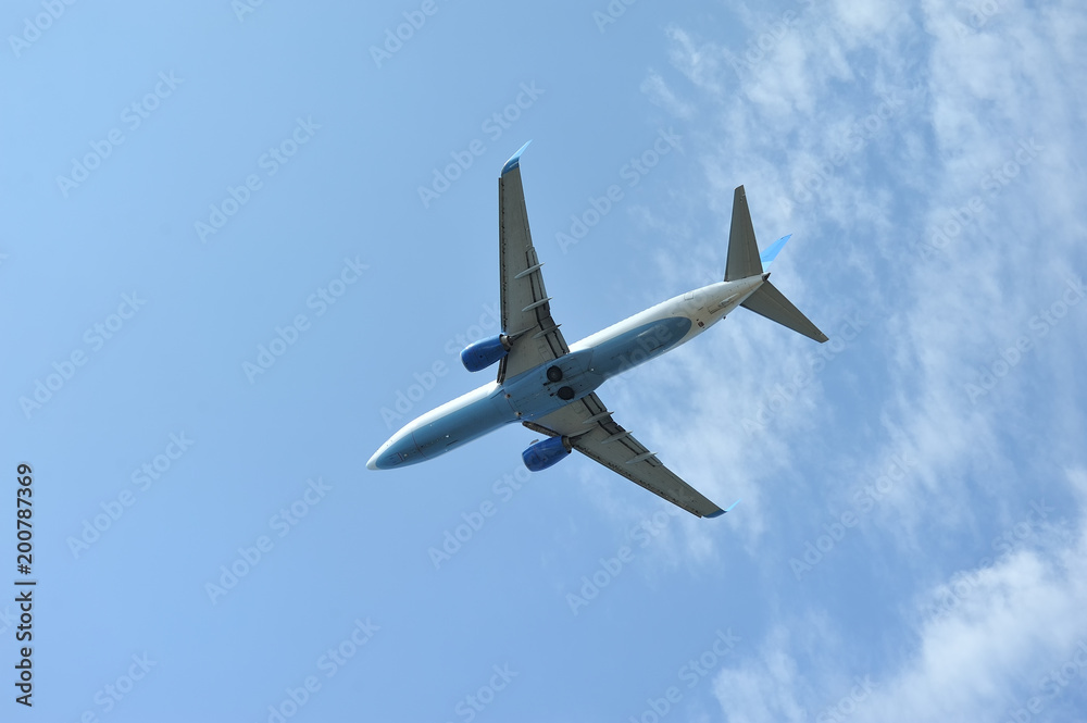 The passenger plane flies low overhead on a blue sky background. Bottom view The passenger plane flies low overhead on a blue sky background. Bottom view