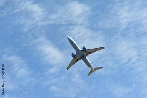 The passenger plane flies low overhead on a blue sky background. Bottom view