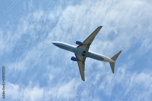 The passenger plane flies low overhead on a blue sky background. Bottom view