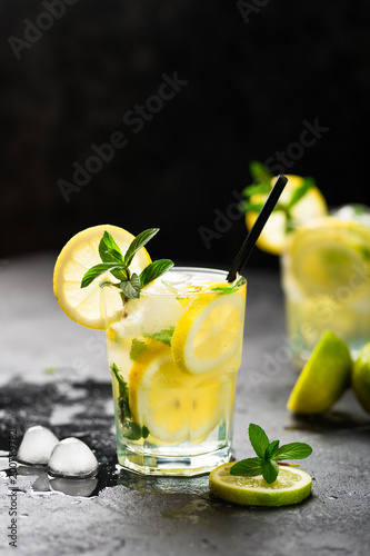 Lemon fruit lime slices caipirinha from Brazil, lemonade mint ice cubes in cold glasses on dark background, alcoholic mojito cockail ice tea green mint leaves, brown sugar spoon, copy space photo