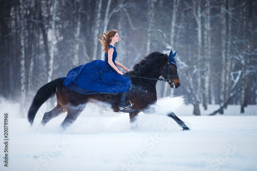 Young girl in blue dress galloping horseback on winter field. Romantic or historical equestrian background with copy space