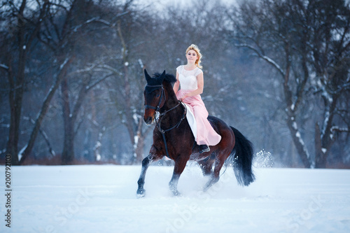 Young woman in pink dress galloping horseback on winter field. Romantic or historical equestrian background with copy space