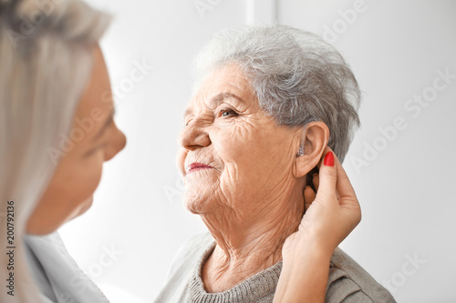 Otolaryngologist putting hearing aid in senior woman's ear on light background photo