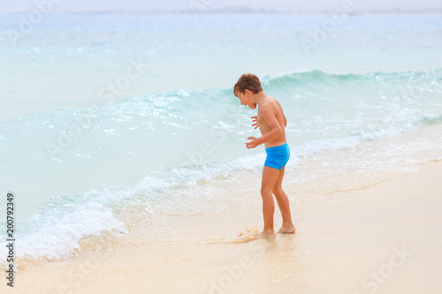 Young boy having fun playing in sea waves on beach. Summer vacation background