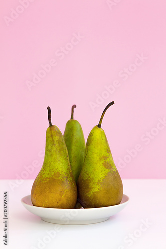three ripe long pears on a saucer on a creative pink background