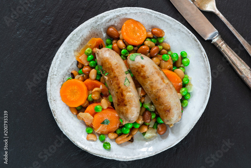 Sausage and bean casserole with carrots and green peas - top view